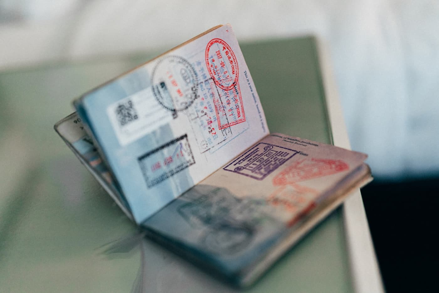 An open, well-travelled passport dense with entry and visa stamps, standing on a table.